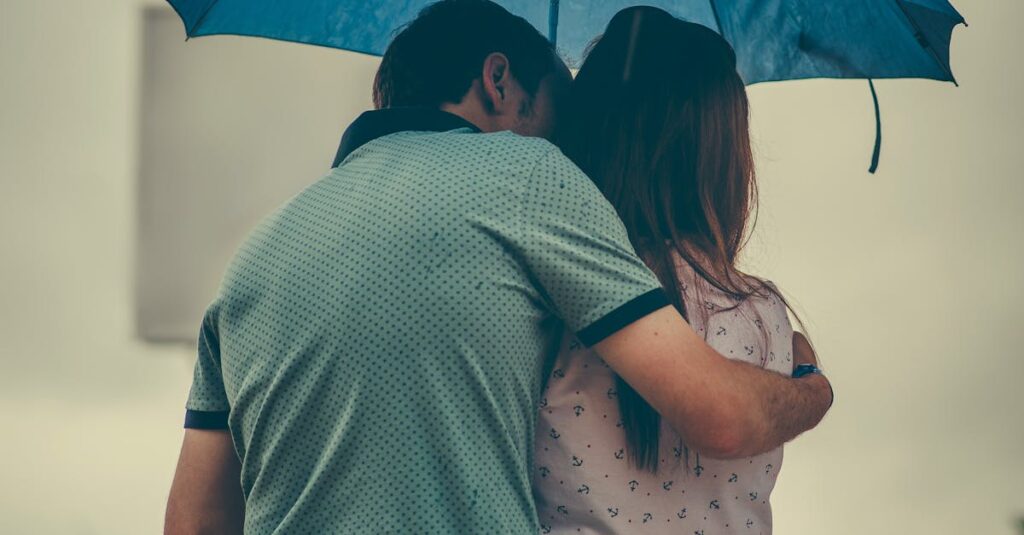 A couple embraces under a blue umbrella in a rainy street scene, evoking love and warmth.
