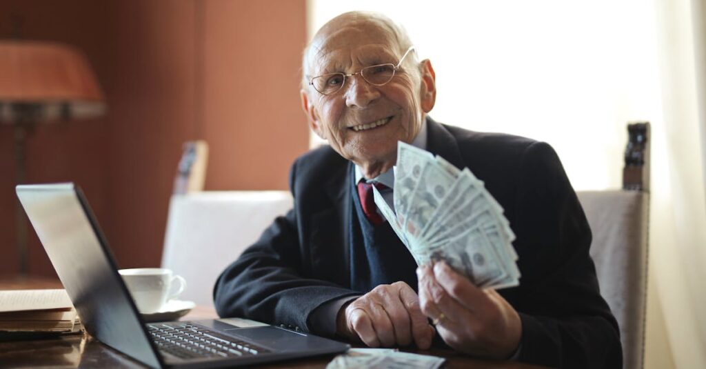 pexels-photo-3823487-3823487 Happy senior businessman showing cash at his desk with a laptop, indoors.