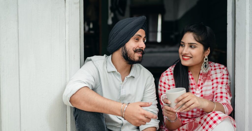 Positive Indian spouses in casual outfits sharing interesting stories while drinking morning coffee on doorstep of house