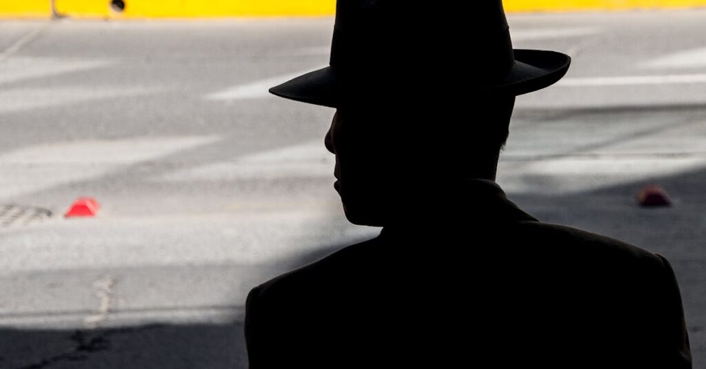 Shadowed silhouette of a man wearing a hat, captured in an urban street setting.