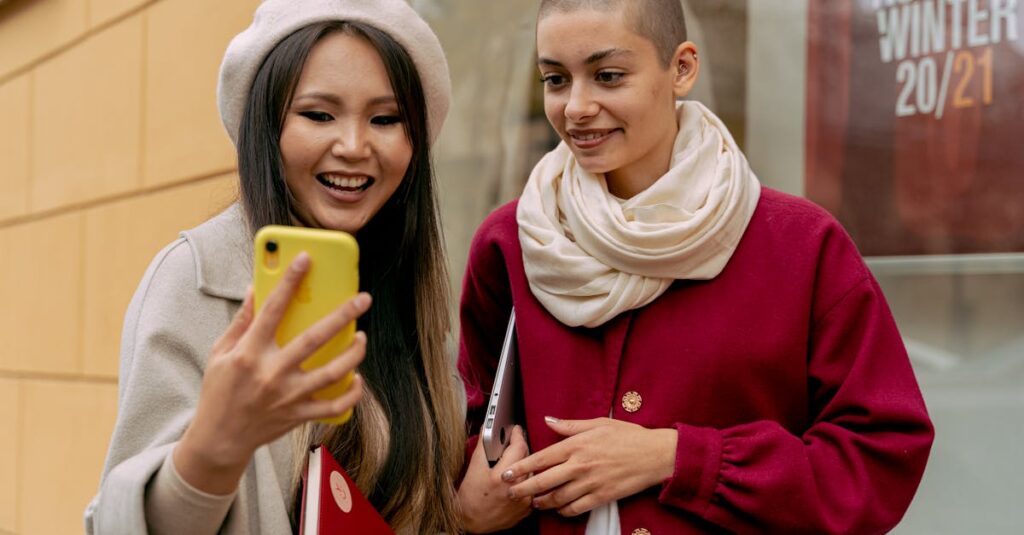Two fashionable women share a happy moment while looking at a phone outdoors. Autumn vibes.