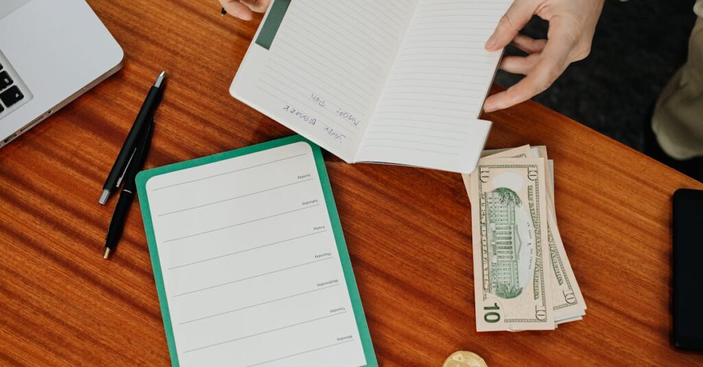 Person organizing budget with notebook and cash on a wooden table, perfect financial planning concept.