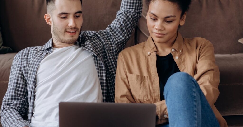 A couple sitting on the floor engaged with a laptop indoors.